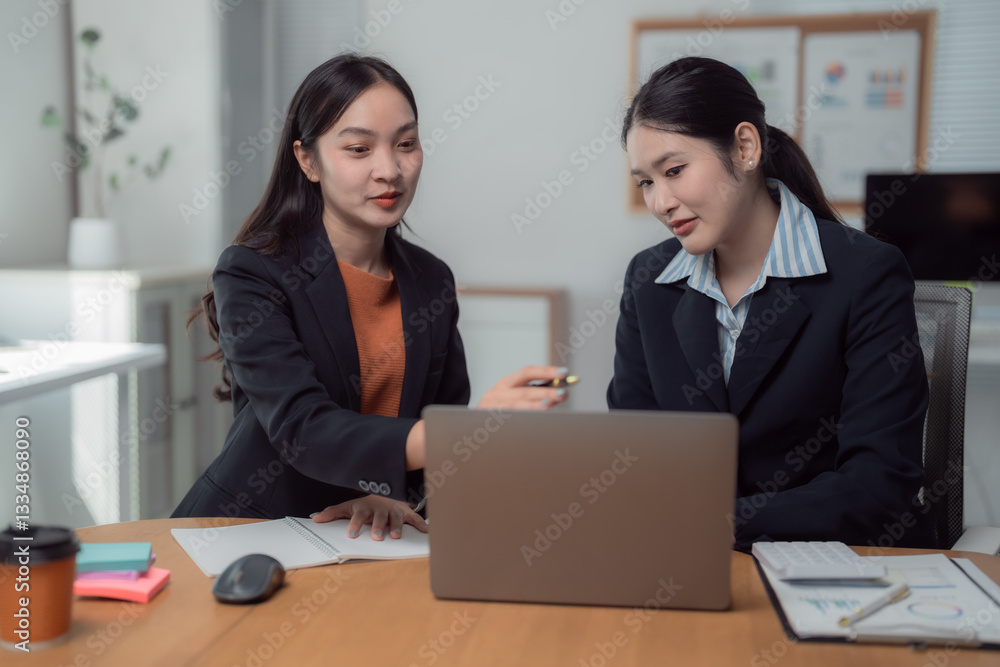 Two asian businesswomen are analyzing financial data on a laptop, collaborating on a project in a contemporary office setting, surrounded by documents and office supplies Two asian businesswomen are analyzing financial data on a laptop, collaborating on a project in a contemporary office setting, surrounded by documents and office supplies