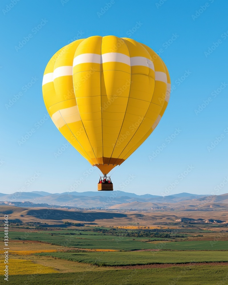 Fototapeta premium Vibrant Yellow Hot Air Balloon Ascending Over Scenic Landscape Under Clear Blue Sky