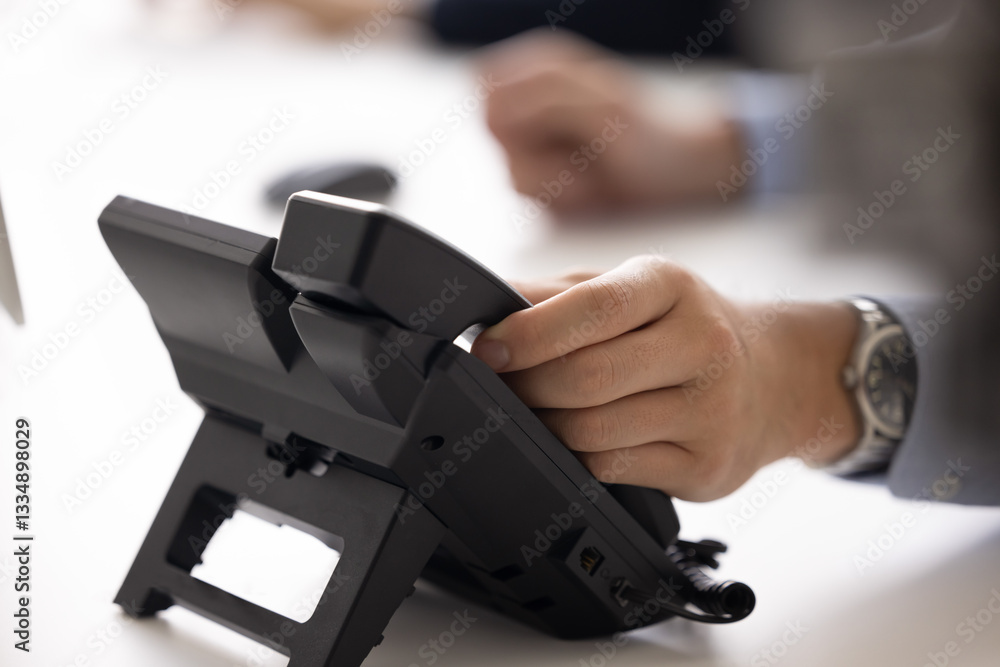 Naklejka premium Hand of businessman touching handset of office landline phone. Office employee, manager, director picking up call, using telephone for business talk, contact, communication. Close up cropped shot
