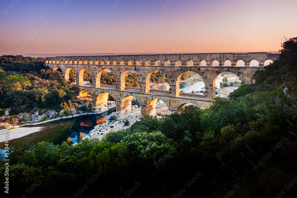 Fototapeta premium Pont du Gard, ancient Roman aqueduct bridge, elevated view, river bend and complete arches, early morning golden light, Gorges du Gardon, natural landscape, UNESCO Biosphere Reserve, Provence, France