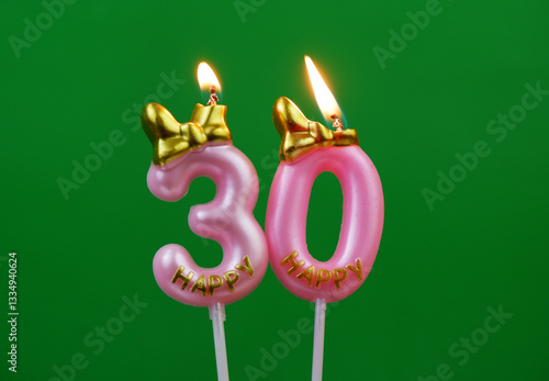 Photography Burning pink birthday candles with golden bow and word happy on green background, number 30