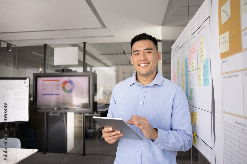 Happy young Asian businessman holding digital tablet, standing in office workspace alone, looking at camera, using modern web technology for project management. Business leader head shot Happy young Asian businessman holding digital tablet, standing in office workspace alone, looking at camera, using modern web technology for project management. Business leader head shot