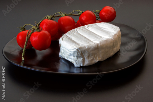 Soft brie cheese with fresh cherry tomatoes on a black plate