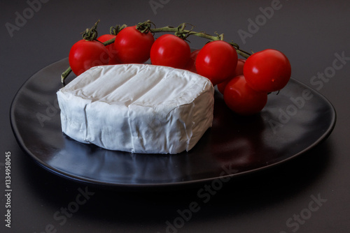 Soft brie cheese with fresh cherry tomatoes on a black plate