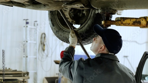 Canvastavla Skilled automotive technician checking vehicle undercarriage with pry bar, weari