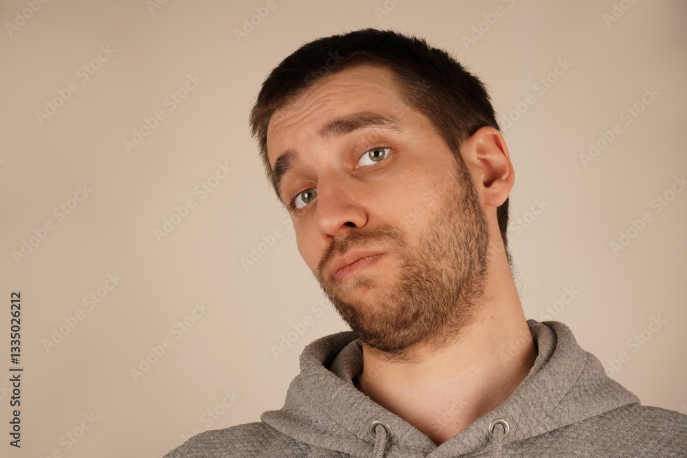 Fototapeta premium Portrait of a man in a gray hoodie, gazing thoughtfully. His green eyes and trimmed beard add detail to his face. The image captures a blend of curiosity and introspection.