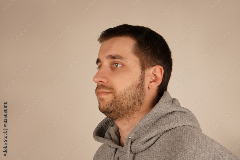 Obraz premium The side view of a man in a grey hoodie highlights his short dark hair and light stubble. His face shows a relaxed demeanor, giving off a casual vibe.