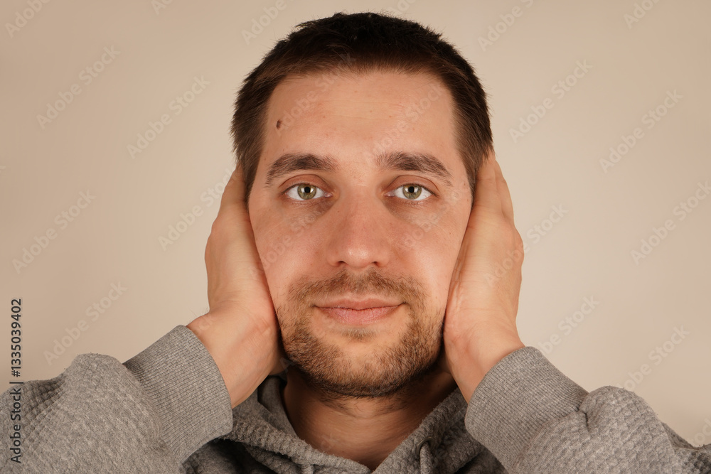 Obraz premium A European man covers his ears with his hands, trying to block out the loud noise. His face shows discomfort. This gesture communicates the frustration and stress he is experiencing.
