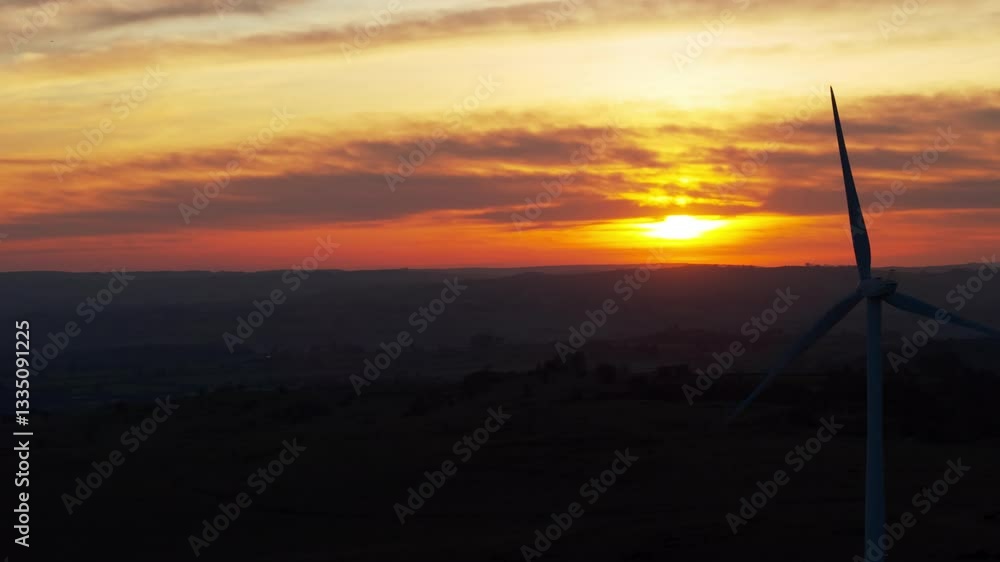 Drone slow-motion view of wind turbines working in a dark landscape at dusk with orange, yellow hues Drone slow-motion view of wind turbines working in a dark landscape at dusk with orange, yellow hues