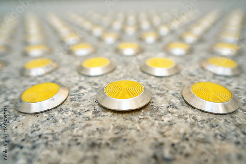 Obraz na płótnie Row of tactile paving dots on textured surface providing guidance, safety for visually impaired pedestrians in an urban environment, selective focus. Close-up of tactile paving with yellow metal bumps w salonie
