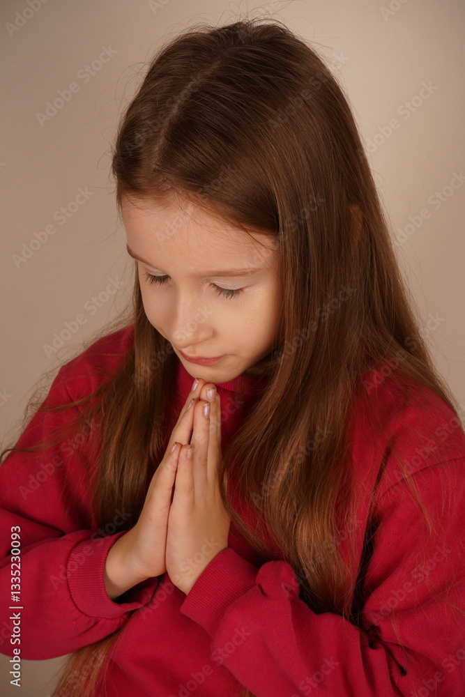 Her calm expression and flowing hair evoke innocence and peace. A tender and sincere moment is beautifully captured. A young girl with long red hair clasps her hands together as if in prayer. Her calm expression and flowing hair evoke innocence and peace. A tender and sincere moment is beautifully captured. A young girl with long red hair clasps her hands together as if in prayer.