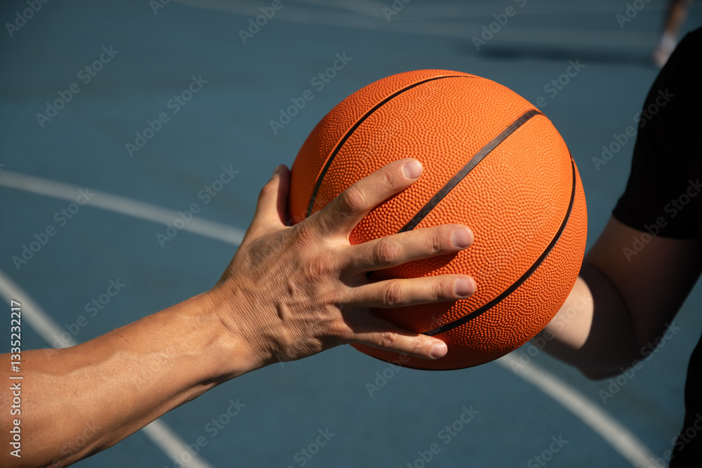 Hands of two basketball players holding orange ball on sports court. Sports goals competition game, champion outdoor workout. Game moment. Close up.