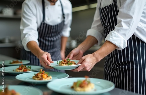 Chef teaches assistant how to arrange meal on plate. Young cook learning to put dish on plate in right way. Training in commercial kitchen. Pro cooking, haute cuisine.