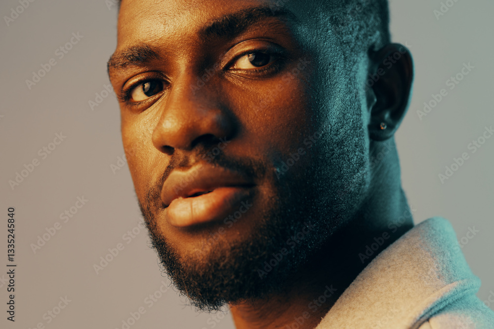 Obraz premium Portrait of a confident Black male model with a stylish haircut, showcasing warm skin tones and thoughtful expression, against a soft gradient backdrop