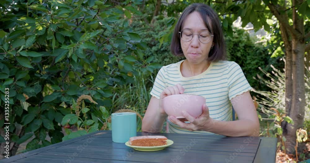 Woman sits at the table eating food outdoor in backyard garden
