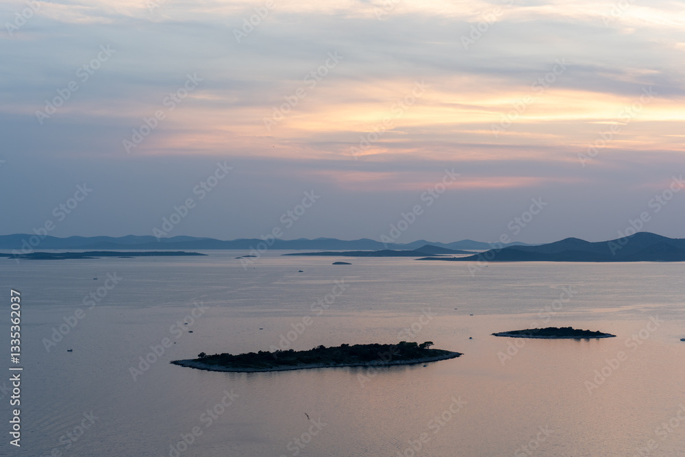 Obraz premium Peaceful coastal panorama with small islands and calm sea at dusk, highlighted by colorful sunset. Concept of natural beauty, serenity, and remote getaway destinations.