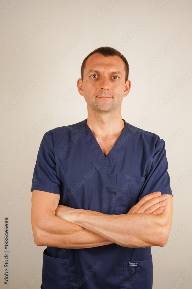 His focused expression highlights professionalism and dedication. The image captures confidence and expertise in the medical field. A man in dark blue medical scrubs poses for a close-up photo. His focused expression highlights professionalism and dedication. The image captures confidence and expertise in the medical field. A man in dark blue medical scrubs poses for a close-up photo.