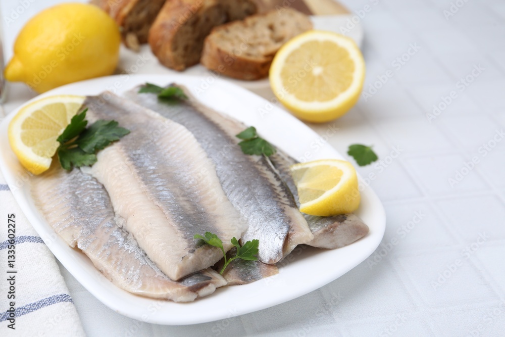 Marinated herring fillets with lemon and parsley on white tiled table, closeup Marinated herring fillets with lemon and parsley on white tiled table, closeup