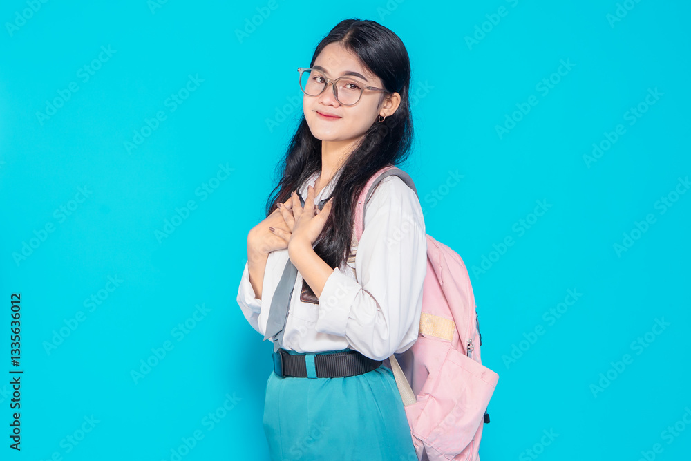 An Indonesian high school student with glasses, a school uniform, and a backpack, smiling warmly while placing her hands on her chest, expressing gratitude against a bright blue background. An Indonesian high school student with glasses, a school uniform, and a backpack, smiling warmly while placing her hands on her chest, expressing gratitude against a bright blue background.