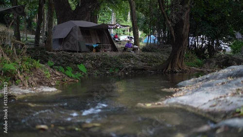 nature camping ten relaxing with water stream slow motion flow and camper on evening to under big tree at garden forest lan sang waterfall national park campground Thailand on holiday vacation travel