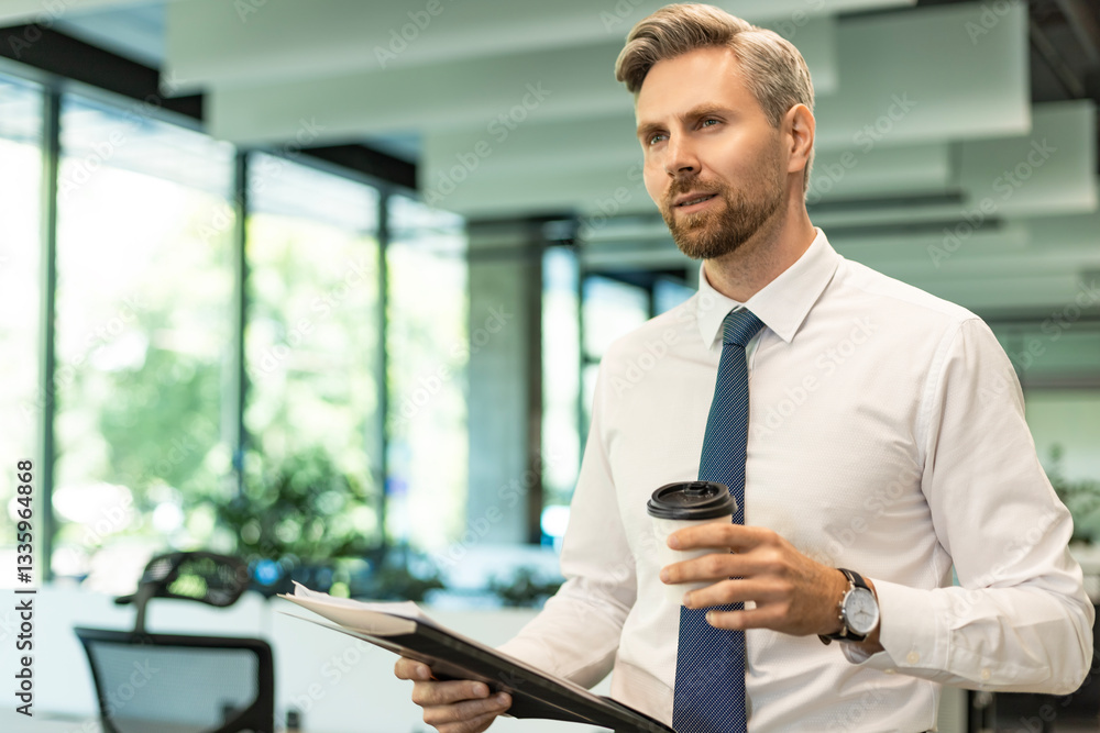 Businessman walking in office corridor with documents and takeaway coffee Businessman walking in office corridor with documents and takeaway coffee