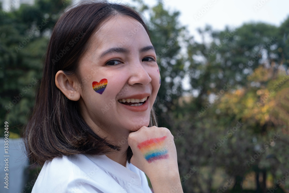A young woman joyfully displays her colorful pride face paint outdoors, radiating positivity and acceptance under a sunny sky. A young woman joyfully displays her colorful pride face paint outdoors, radiating positivity and acceptance under a sunny sky.