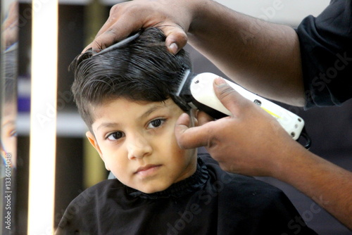 Boy is getting his haircut done at salon. Barber is cutting hair of a 4 year old cute little boy at barber shop. little child is enjoying his new hair style and hair cut. Boy is looking very smart. 