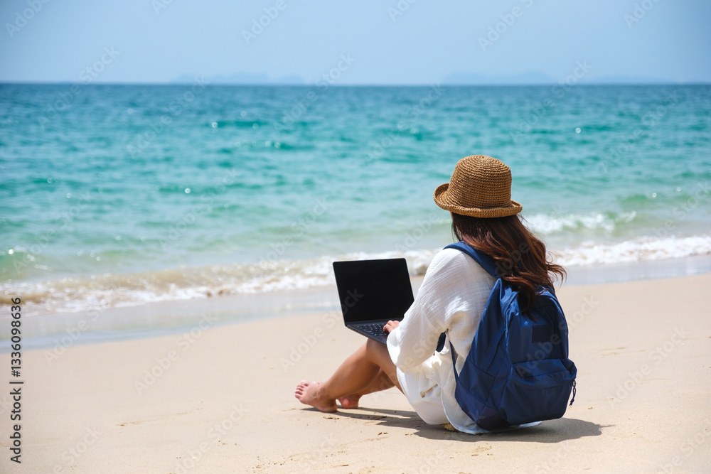 A female traveler using and working on laptop computer while sitting on the beach A female traveler using and working on laptop computer while sitting on the beach