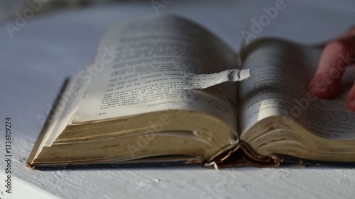 Detailed view of an old book as pages are being flipped and removed by a person's hands