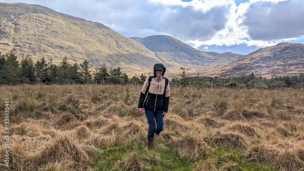 Beautiful woman backpacker in hooded jacket hiking at river Erriff near Aesleagh, county Mayo, Ireland, Irish landscape, mountains and nature background