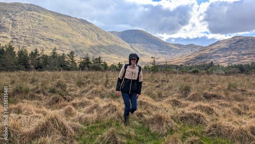 Obraz na płótnie Beautiful woman backpacker in hooded jacket hiking at river Erriff near Aesleagh, county Mayo, Ireland, Irish landscape, mountains and nature background w salonie