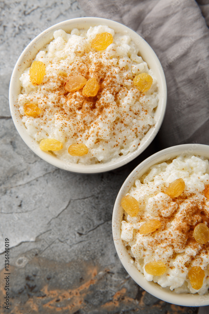 Creamy Rice Pudding with milk and sugar, then finish with cinnamon, vanilla and raisins closeup on the bowl on the table. Vertical top view from above
