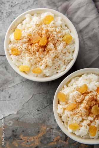 Creamy Rice Pudding with milk and sugar, then finish with cinnamon, vanilla and raisins closeup on the bowl on the table. Vertical top view from above