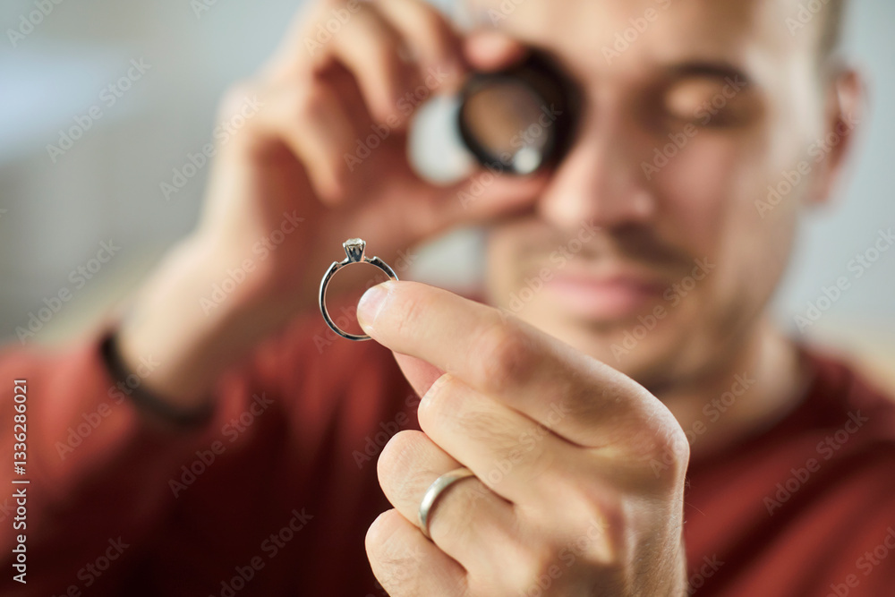 Closeup portrait of young man jeweler looking through magnifying glass examining gold ring evaluating jewelry with diamond. Jewellery appraiser working with jewel. Selective focus. Closeup portrait of young man jeweler looking through magnifying glass examining gold ring evaluating jewelry with diamond. Jewellery appraiser working with jewel. Selective focus.