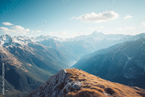 Majestic mountain landscape showing valley and snowy peaks under blue sky.