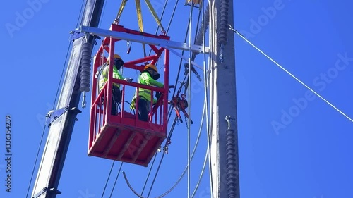 Two skilled workers on a lift are ensuring safety during electrical maintenance on tall pole