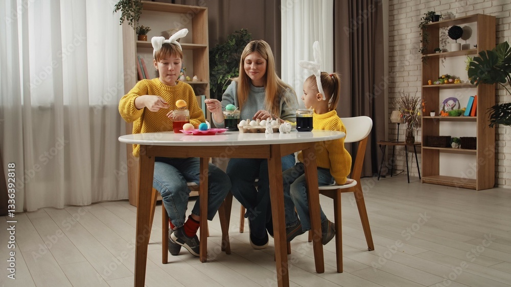 Mother and little daughters preparing for easter celebrations, sitting at table and making colored eggs with ink and water, smiling and having fun together. Mother and little daughters preparing for easter celebrations, sitting at table and making colored eggs with ink and water, smiling and having fun together.