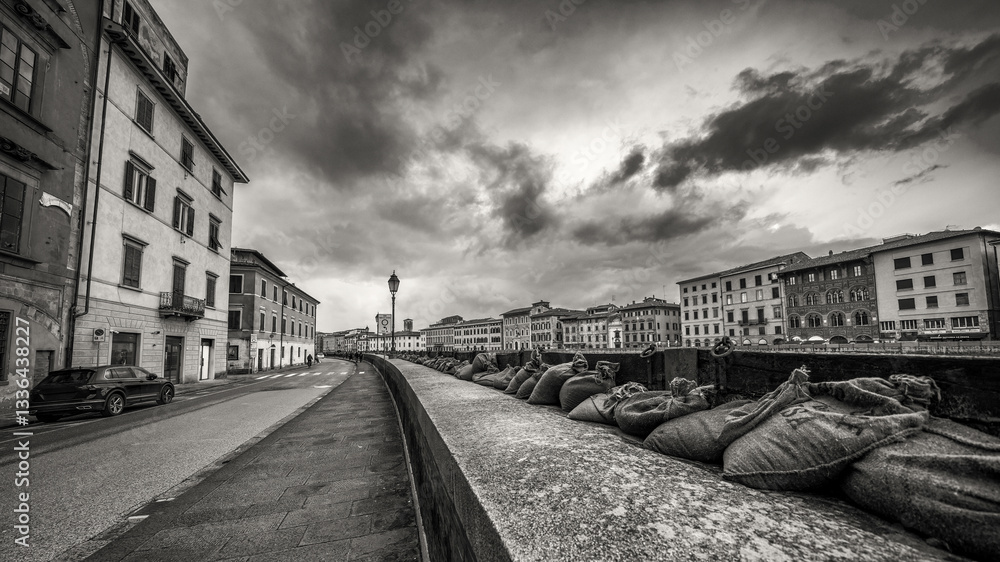 Dramatic view of the swollen Arno River at sunset with flood defenses along Pisa’s Lungarni