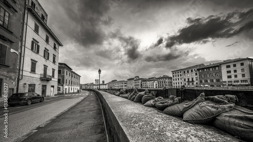 Dramatic view of the swollen Arno River at sunset with flood defenses along Pisa’s Lungarni