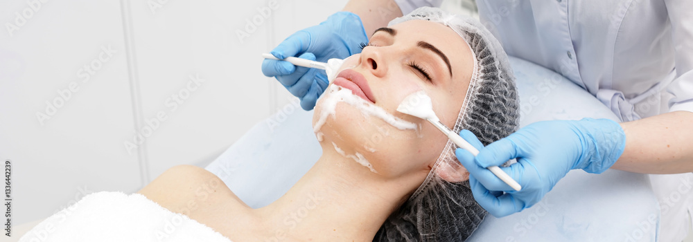 Fototapeta premium Close-up of a young woman undergoing a facial skincare treatment. A cosmetologist applies a carboxytherapy product. Concept of peeling, cosmetic cleanses, and skin rejuvenation.