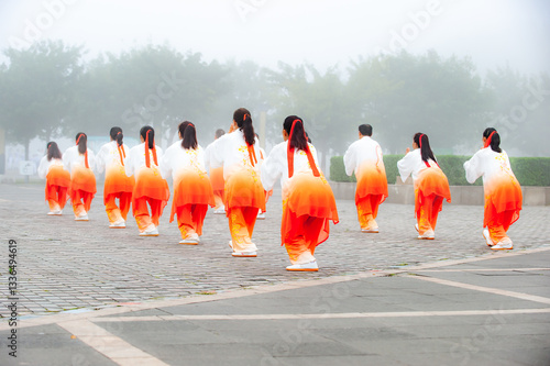 In the foggy morning at the park square, people engage in Tai Chi fitness exercises