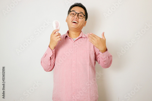 Adult Asian man using electric hand fan and showing swelter gesture
