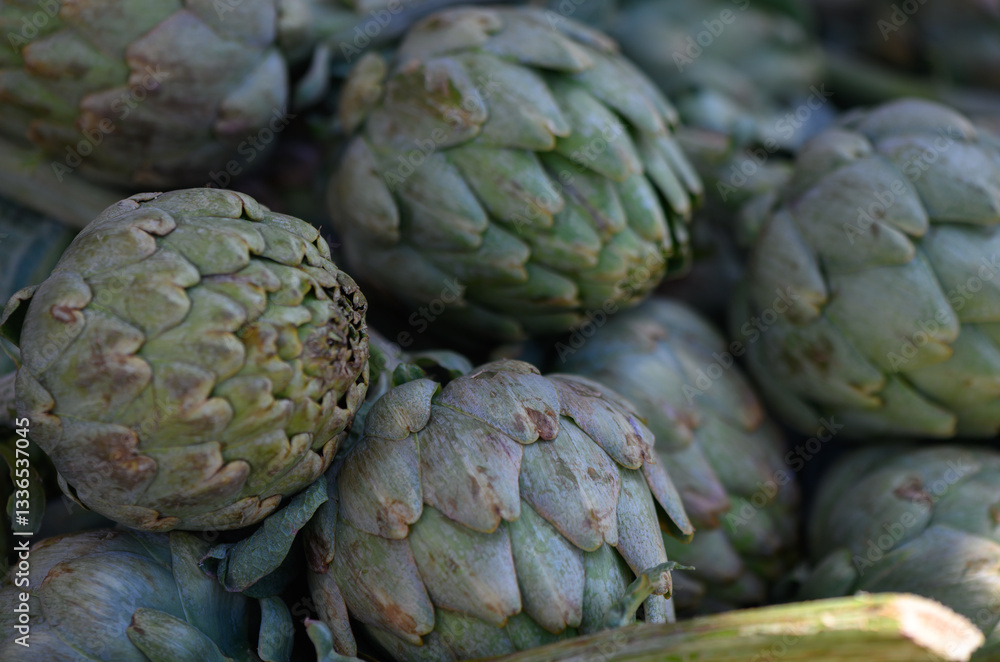 Obraz premium Artichokes piled together in a vibrant farmers market during sunny spring