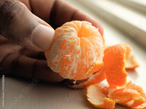 Hand Holding Peeled Citrus: Focus on a peeled citrus fruit, revealing its segments, held by a human hand.