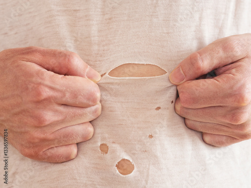 A man inspecting a ripped t-shirt that he is wearing. Close up.