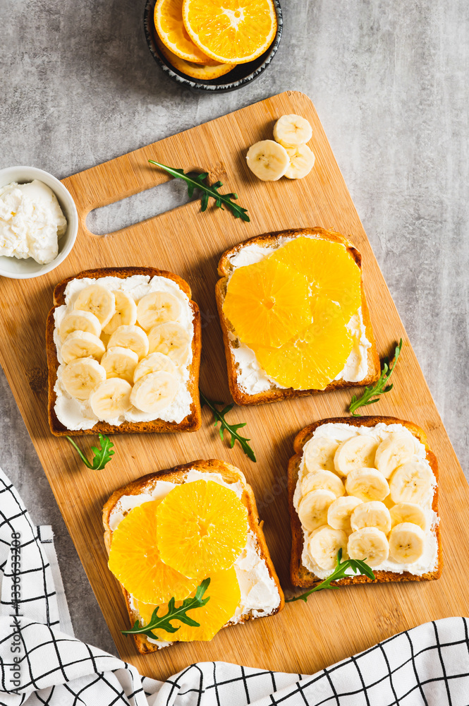 Sandwiches with ricotta, orange and banana on a board on a table top and vertical view