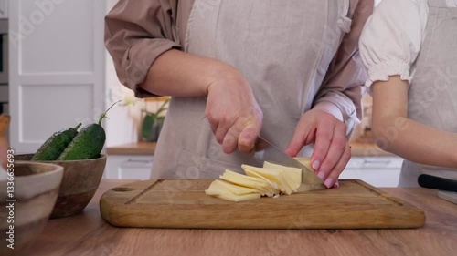 A woman cuts cheese. A girl and her mother are preparing a bright vegetable salad in a cozy kitchen.