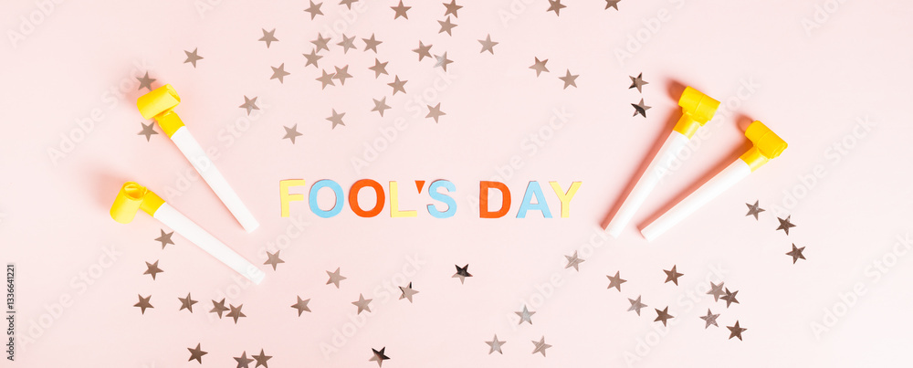 April Fools' Day written in colored letters, whistles and stars on pink top view web banner