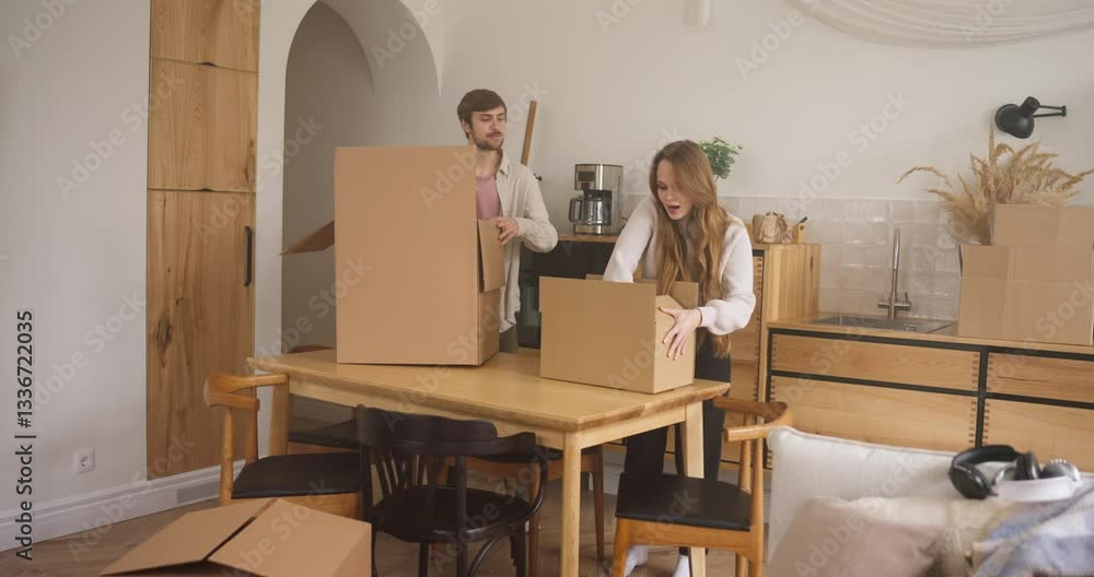 A happy blond guy with stubble and his blonde girlfriend collect things and put them in large cardboard boxes in the process of moving A happy blond guy with stubble and his blonde girlfriend collect things and put them in large cardboard boxes in the process of moving