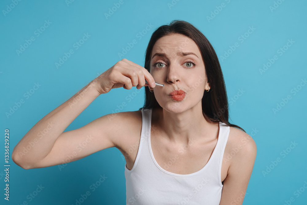 Woman plucking her mustache with tweezers on light blue background Woman plucking her mustache with tweezers on light blue background